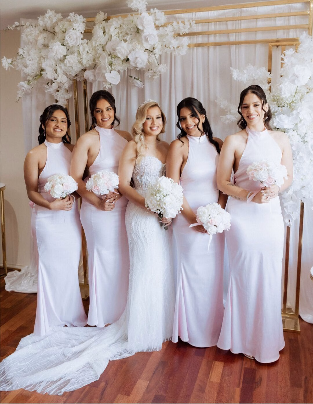 Bride with her bridesmaids beneath a white floral arch